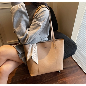 Close-up of beige lychee leather tote bag with decorative silk scarf and shoulder strap