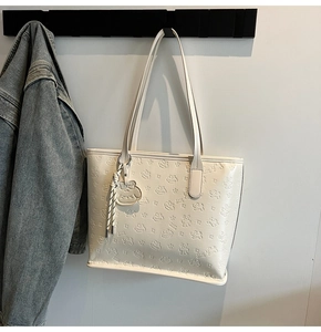 Détail d'un sac cabas beige avec motifs d'ours en relief et breloque assortie sur crochet