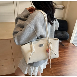 Detail view of cream white pleated tote bag with silver logo plate and heart pendant