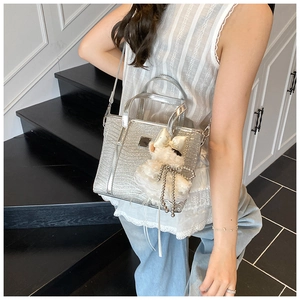 Close-up of silver tote bag with crocodile texture and cute white plush dog charm