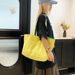 Détail du sac cabas en toile jaune avec broderie chien vert porté par un mannequin