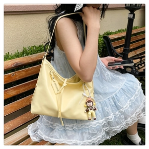 Detail of light yellow shoulder bag with a cute cartoon doll charm and MASHK brand tag