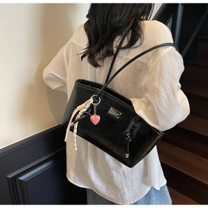 Detail of glossy black crinkled tote bag with silver logo and pink heart charm accessory