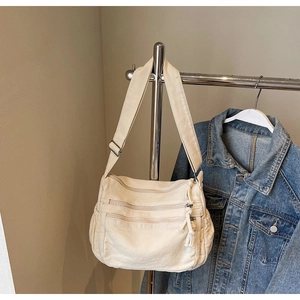 Detail of off-white canvas crossbody bag with multi-pocket zipper design and adjustable strap