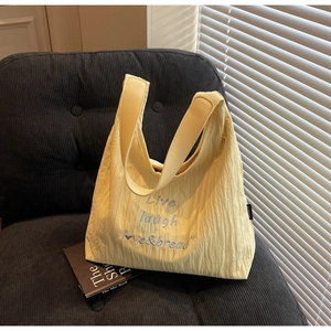 Detail of light yellow pleated tote bag with Live laugh love embroidery on sofa