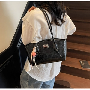 Detail of a shiny black pleated shoulder bag featuring a cute pink heart charm accessory