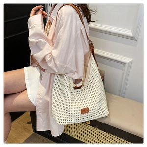 Close-up of a beige hollow-out woven straw tote bag with brown leather handle strap