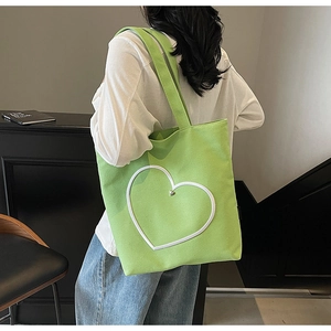Gros plan d'un sac cabas en toile verte avec motif cœur porté à l'épaule par un mannequin
