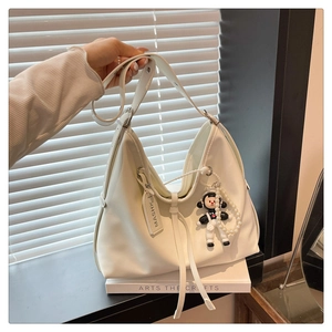 Detail of white leather hobo bag with astronaut charm and pearl chain accessory