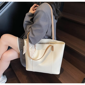 Close-up of beige leather tote bag with brown straps and elegant decorative silk scarf