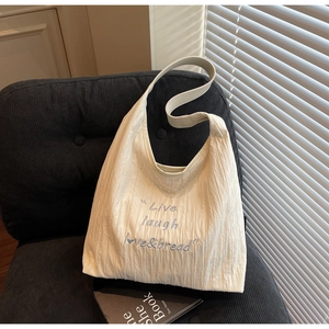 Detail of beige pleated tote bag with blue embroidered slogan on a grey velvet seat