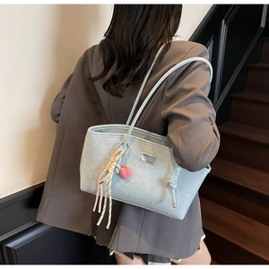 Detail view of light blue tote bag with heart charm and silver plaque on shoulder strap
