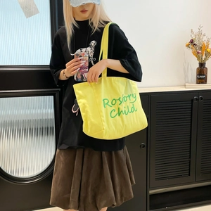 Détail d'un sac cabas en toile jaune avec broderie verte porté par un mannequin