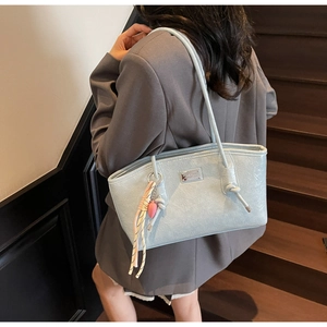 Detail of light blue tote bag featuring pleated texture, metal logo, and rainbow scarf accent