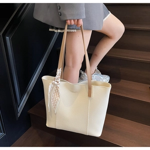 Close-up of beige lychee leather tote bag with silk scarf on handle and brown shoulder strap