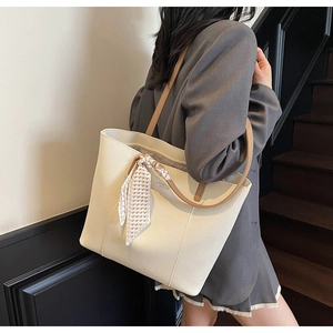 Macro view of cream-colored pebble leather tote bag with silk scarf on handle