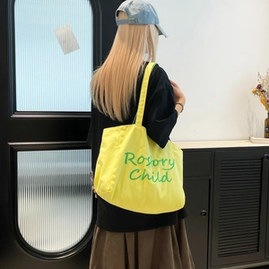Détail d'un sac cabas en toile jaune avec broderie verte Rosary Child sur la surface