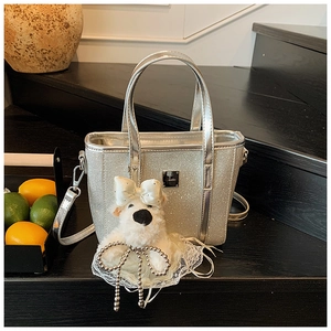 Detail of silver glitter bucket bag with plush puppy charm on a wooden display