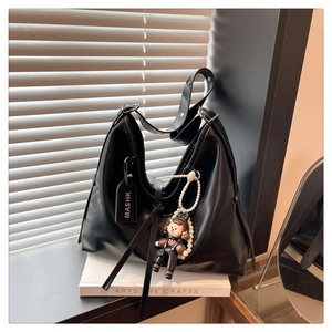 Detail of black PU hobo bag featuring wide adjustable strap and pearl doll charm