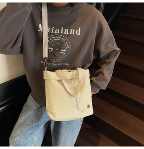 Detail of light beige canvas bucket bag with drawstring closure and metal logo on stairs