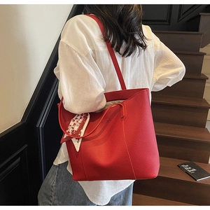 Detail of red pebbled leather tote bag with silk scarf on handle worn by model