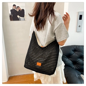 Detail of black crochet tote bag featuring leather logo patch and woven mesh texture