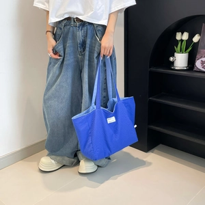 Détail d'un grand sac cabas bleu en maille gaufrée avec étiquette blanche décorative