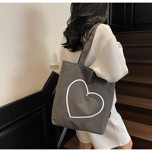 Détail du cabas en toile grise avec un grand patch cœur blanc et un petit cœur en métal argenté