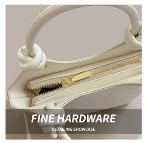 Détail du sac en cuir blanc avec fermeture éclair dorée et nœud décoratif sur la poignée
