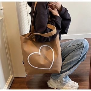 Détail d'un sac cabas en toile marron avec contour de cœur blanc tenu par un mannequin