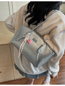 Metallic silver pleated tote bag with pink heart charm and knot details on a model