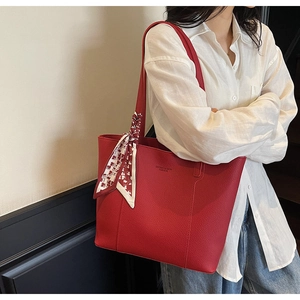Detail of red leather tote bag with silk scarf on handle and branded fashion lettering