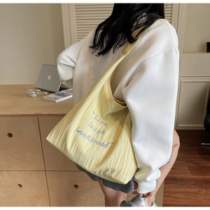 Detail of yellow pleated tote bag with blue embroidery shown in a casual lifestyle setting