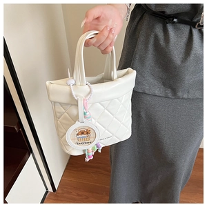 Detail of white quilted handbag featuring Capybara charm and intricate embroidery texture