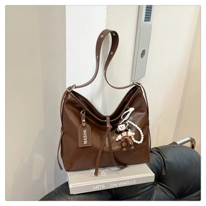 Detail of a brown leather tote bag with MASHK tag and pearl doll charm on books