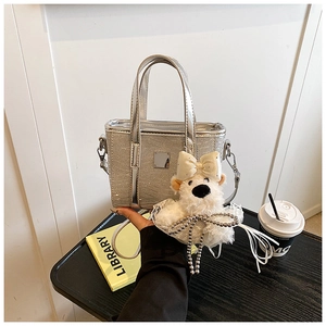 Detail of silver sequin bucket bag featuring a cute plush bear pendant on black wood