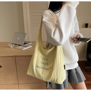 Detail of light yellow pleated tote bag with blue 'Live laugh love' embroidery and soft texture