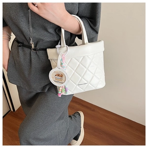 Detail view of white quilted handbag featuring a cute Capybara charm and side branding