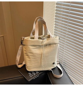Detail view of beige nylon bucket bag with drawstring closure on a black leather chair