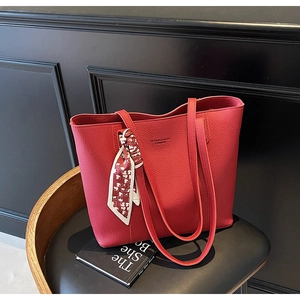 Detail of red lychee leather tote bag featuring decorative heart scarf on black seat