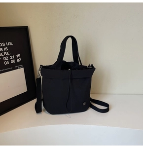 Detail of minimalist black bucket bag with drawstring closure and metal logo on a white desk