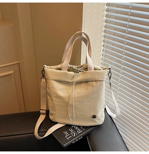 Close-up of cream nylon bucket bag with drawstring closure and strap on a leather sofa