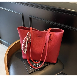 Detail of red lychee grain leather tote bag with gold logo and decorative silk scarf