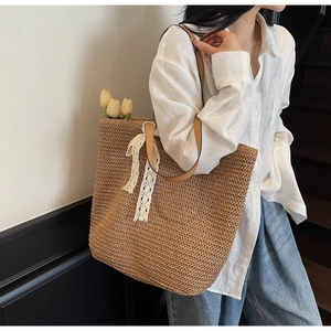 Detail of dark brown woven straw tote bag with brown leather straps and white lace bow