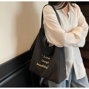 Dettaglio della borsa tote nera plissettata con ricamo bianco e design minimalista