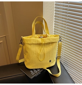 Detail of yellow pleated fabric texture on bucket bag with drawstring and metal logo