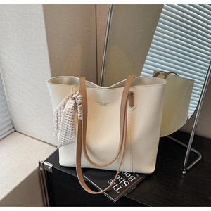Close-up of beige leather tote bag with silk scarf detail and branded fashion text