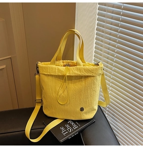 Detail of yellow drawstring bucket bag with textured fabric and metal logo on a book