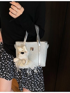 Silver sequin bucket bag with cute dog pendant shown in a stylish outdoor setting