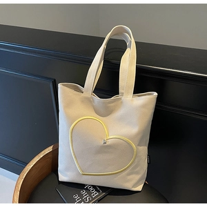 Gros plan d'un sac cabas en toile beige avec broderie cœur jaune et rivet métallique argenté
